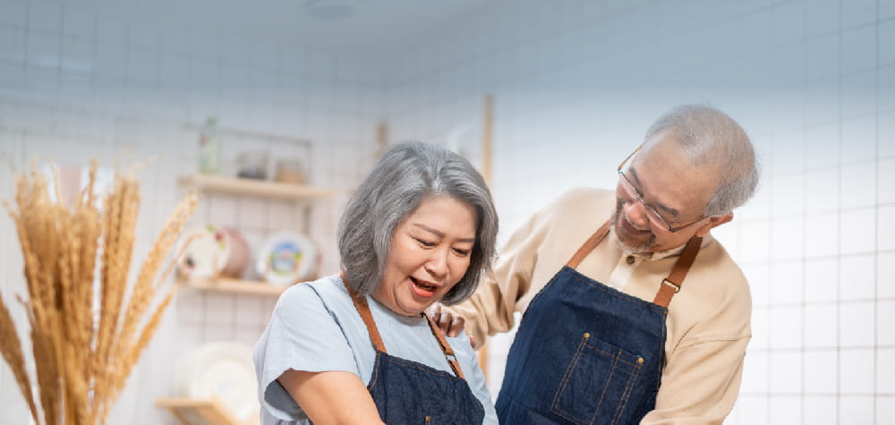 elderly retired asian couple aging in place in-home cooking in aprons