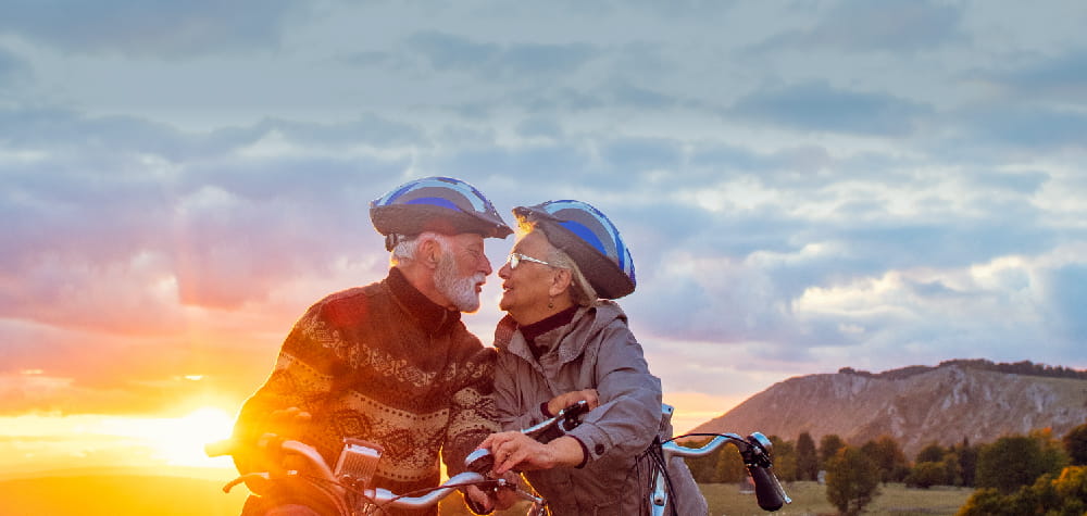 Elder retired white couple elder care planning bicycle helmets sunset kissing