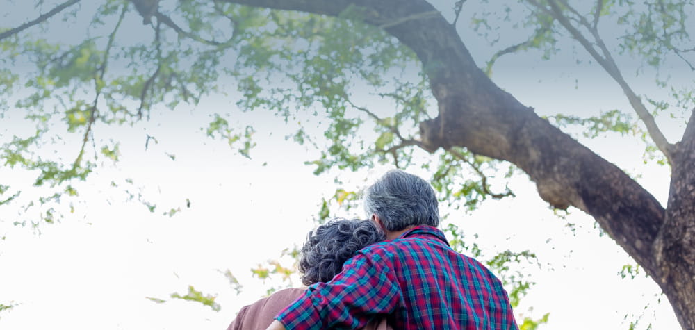 Retired couple in assisted living independent living facility hugging under tree