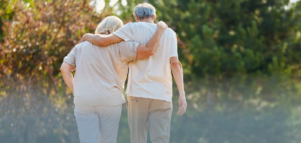 Elder retired white couple dementia care planning walking toward woods
